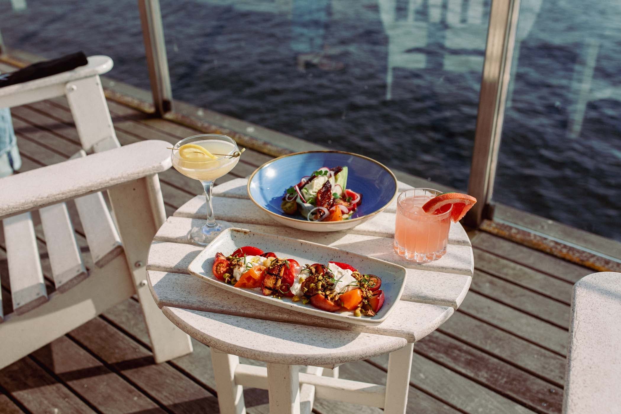 A baratta salad, 2 cocktails and an avocado dish on a balcony of a room at Edgewater