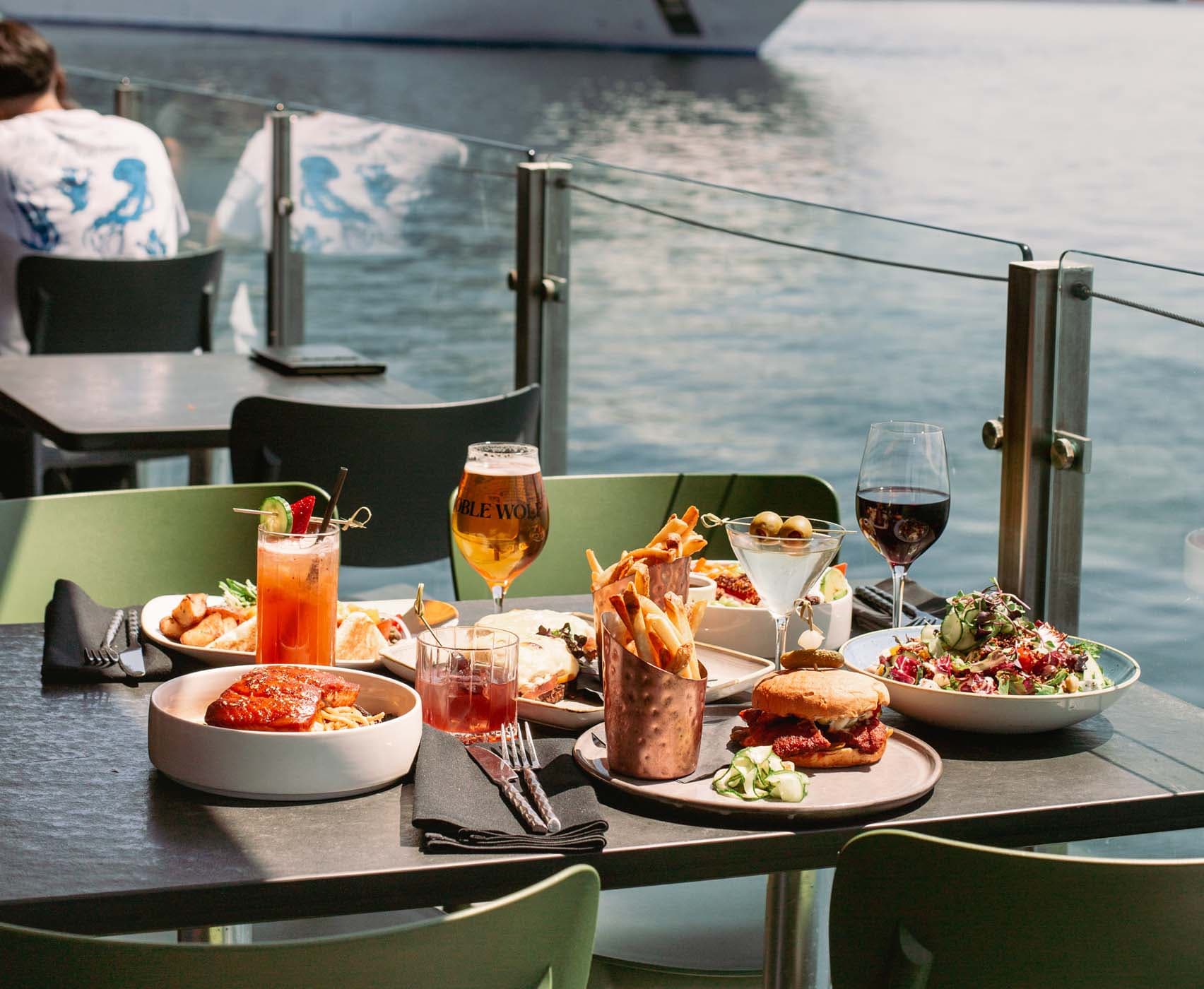 A spread of different American style dishes on a patio table at Edgewater with a cruise ship in the distance
