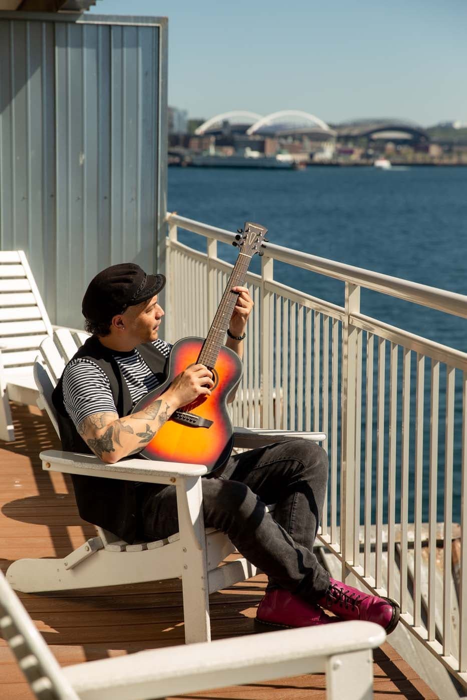 A man playing guitar on a room balcony over looking the water at Edgewater