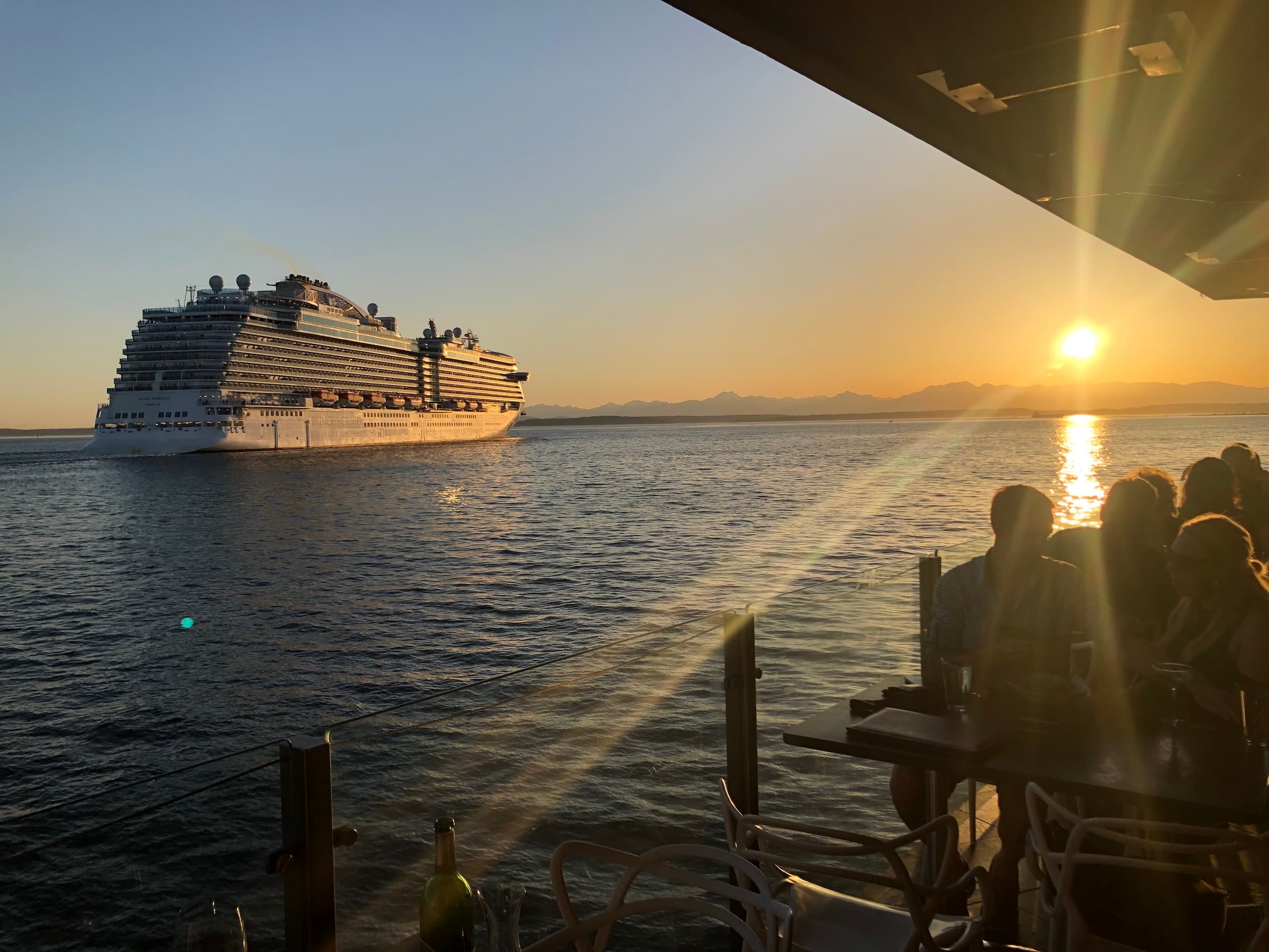 People on a restaurants patio looking over the water at a cruise ship
