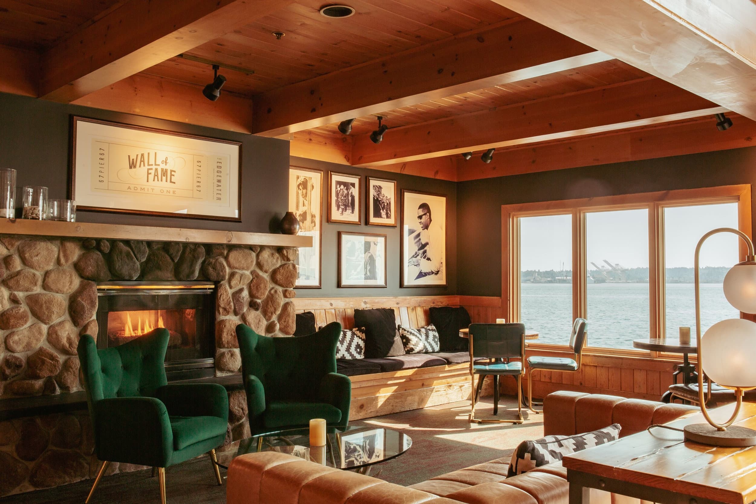 Fireside lounge at The Edgewater Hotel in Seattle, with green velvet armchairs, a river-rock fireplace, a rock ’n’ roll Wall of Fame and views of Elliott Bay