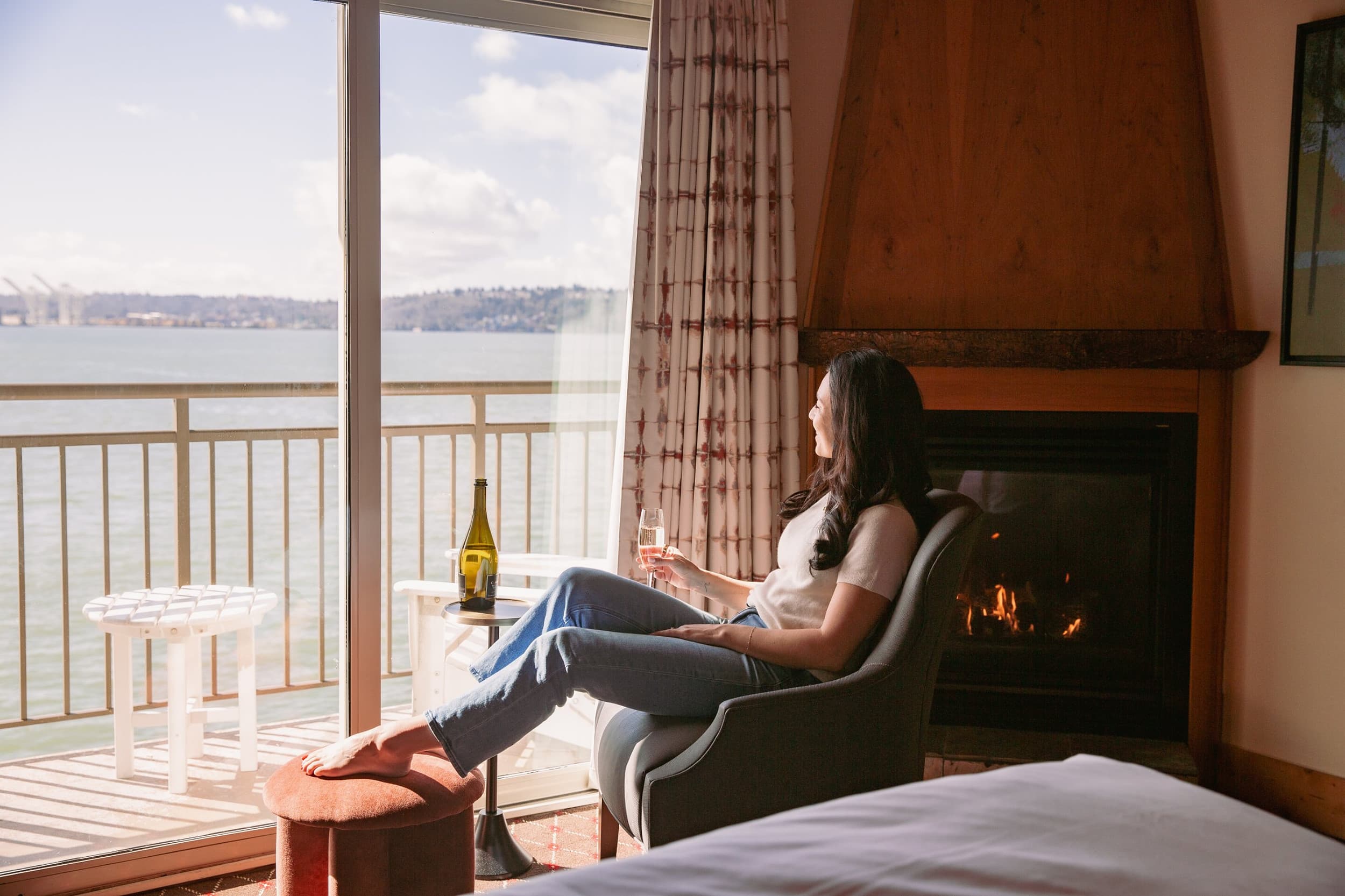 Guest relaxing by the fireplace in a waterfront room at The Edgewater Hotel Seattle, with a private balcony overlooking Elliott Bay